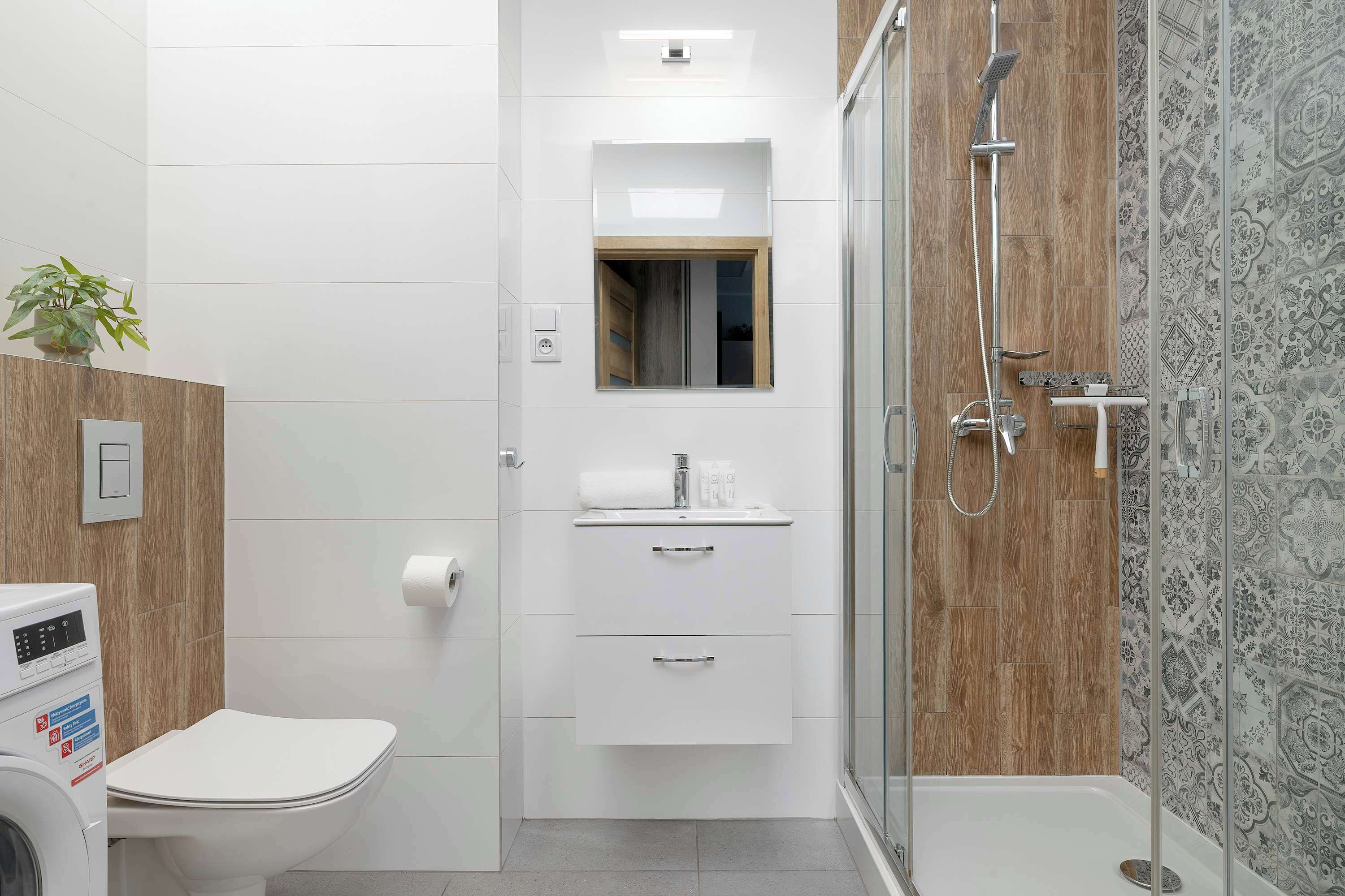 Un baño moderno con inodoro, ducha, lavabo con espejo y lavadora empotrada.