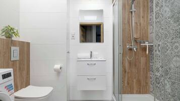 Un baño moderno con inodoro, ducha, lavabo con espejo y lavadora empotrada.