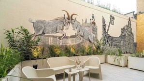 A modern outdoor seating area with a mural of two goats and a building.