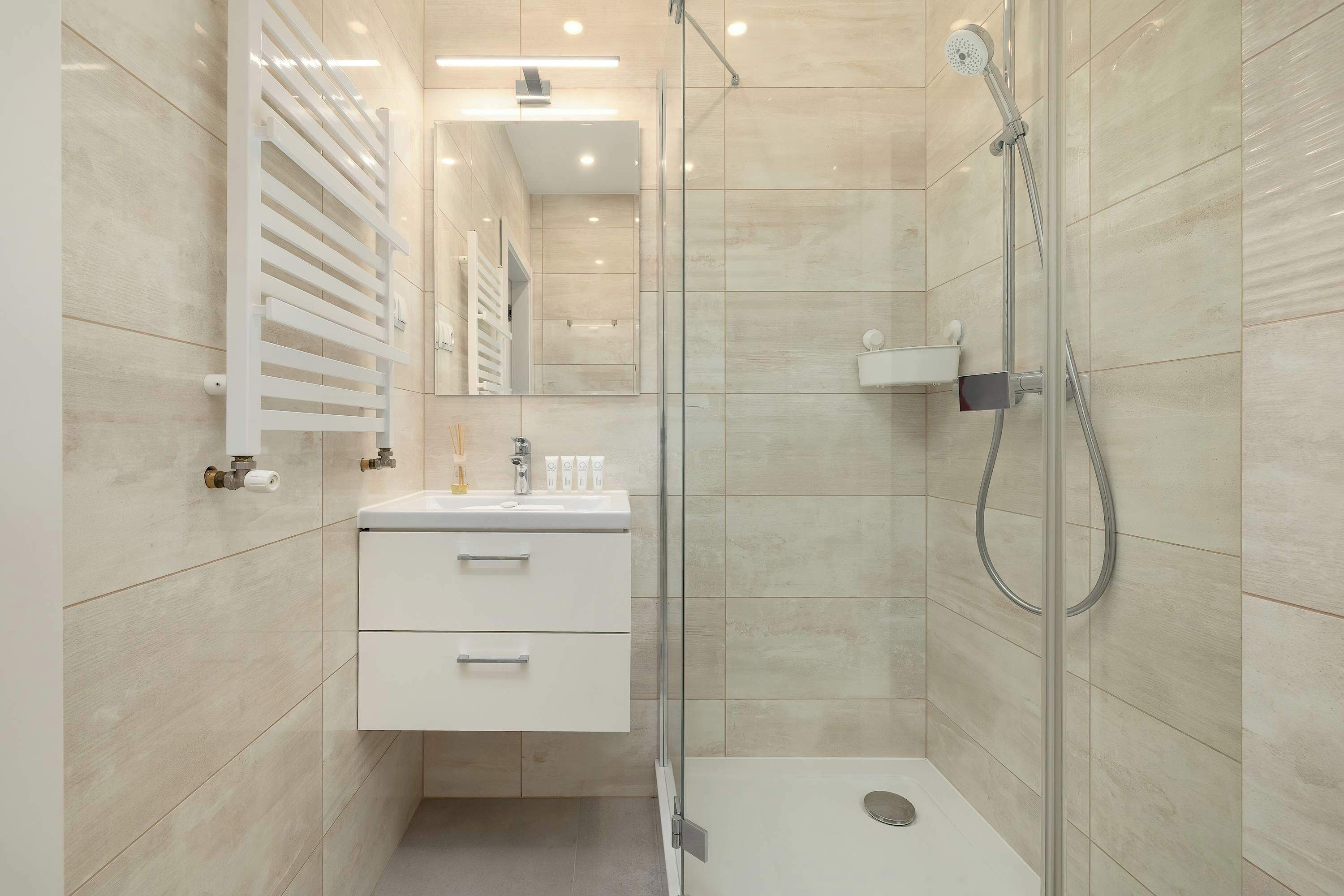 Un baño moderno con ducha envuelta en vidrio, tocador blanco con cajones y un espejo.