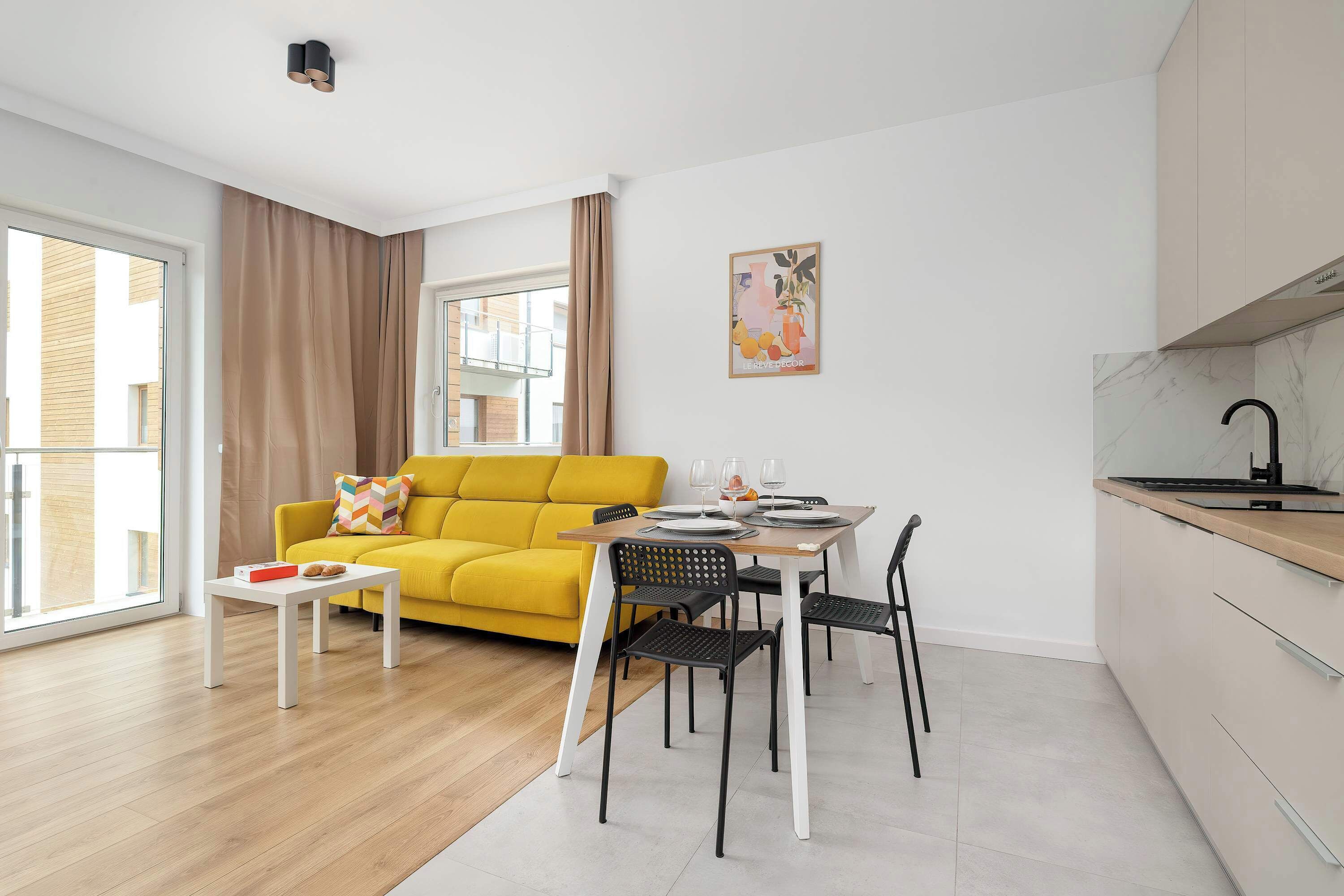 Un espacio habitable moderno con un sofá amarillo, una mesa de comedor con sillas, una zona de cocina y un ventanal grande.