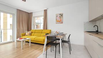 Un espacio habitable moderno con un sofá amarillo, una mesa de comedor con sillas, una zona de cocina y un ventanal grande.
