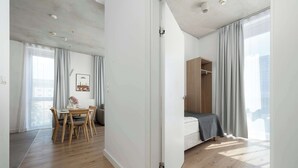 A modern hotel room with a wooden floor, a bed with a gray blanket, a wooden wardrobe, and a dining area with a table and chairs. - Modern Apartment in Center | Air Conditioning | Desk (Wrocław)