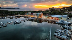 A marina with boats docked, a waterfront building, and a sunset in the background. - Flamingo View Studio (Playa Flamingo)