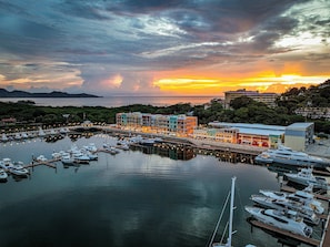 Ein Yachthafen mit vertäuten Booten, ein Gebäude am Wasser und ein Sonnenuntergang im Hintergrund.