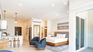 A modern hotel room with a bed, a desk, chairs, a kitchen area, and a sliding glass door to the outside. - Marina View Studio (Playa Flamingo)