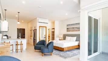 Ein modernes Hotelzimmer mit Bett, Schreibtisch, Stühlen, einer Küchenzeile und einer Glastür zum Außenbereich.