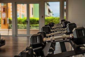 Una hilera de mancuernas negras en un gimnasio con ventanas amplias y vistas a edificios.