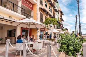 Terraza con sillas blancas y sombrillas, un restaurante llamado 'OCEANA', y un edificio con balcones y barandillas.