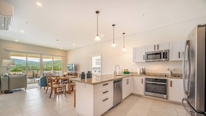A modern kitchen with white cabinets, stainless steel appliances, and a dining area with a view. - Marina View 2 Bedroom Suite (Playa Flamingo)