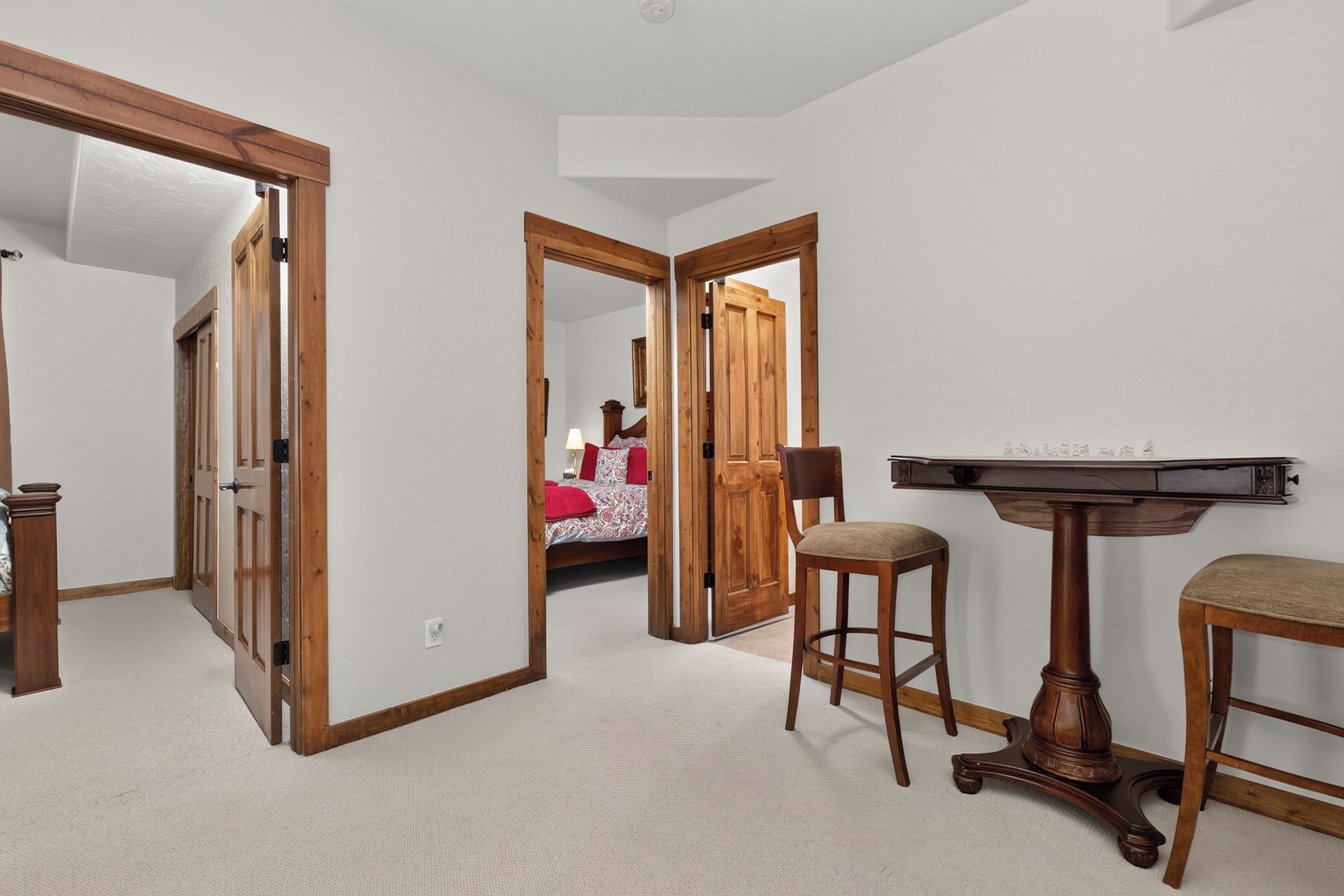 Una habitación con puerta de madera, cama con ropa de cama roja, escritorio con lámpara y una silla.