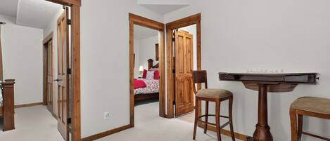 Una habitación con puerta de madera, cama con ropa de cama roja, escritorio con lámpara y una silla.