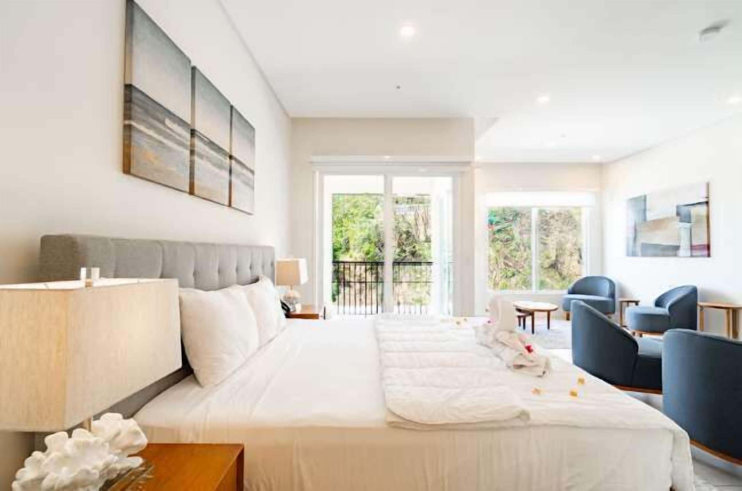 Habitación de hotel con cama, mesita de noche, lámpara y vistas al exterior.