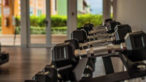 Une rangée de haltères noirs dans une salle de sport dotée de grandes fenêtres et offrant une vue sur les bâtiments environnants.