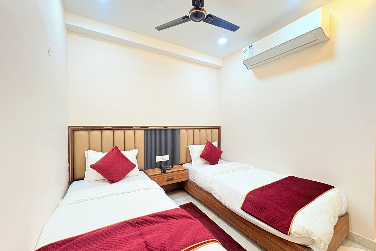 A hotel room with two beds, a ceiling fan, an air conditioning unit, and a bedside table with a phone.