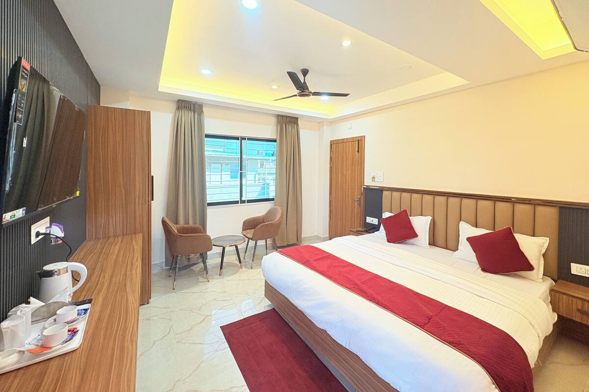 A hotel room with a bed, a desk with a computer, a chair, a small table, and a window.