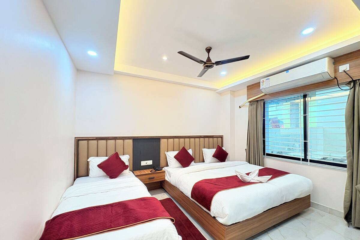 A hotel room with two beds, a ceiling fan, an air conditioning unit, and a window with curtains.