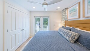 Een slaapkamer met een bed, plafondventilator, witte deuren en ingekaderde foto's aan de muur.