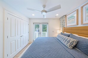 Ein Schlafzimmer mit einem Bett, Deckenventilator, weißen Türen und gerahmten Bildern an der Wand.