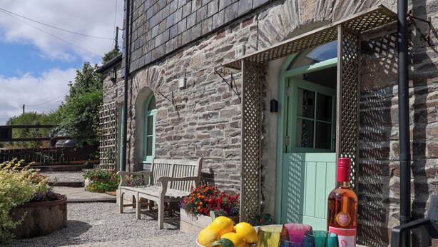 A stone building with a bench and a table with a bowl of fruit and wine glasses. - Linhay Barn (Saltash)
