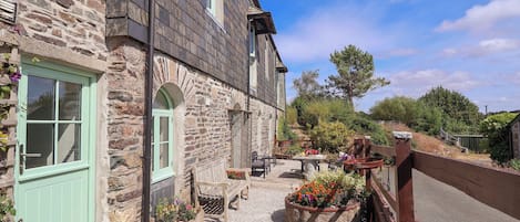 A stone building with a green door, outdoor seating, and flower beds.
