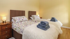 A double bed with floral bedding, a wooden nightstand with a lamp, and a fluffy white rug. - Linhay Barn (Saltash)