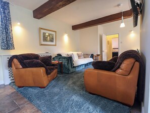 Ein Wohnzimmer mit einer Couch, zwei Sesseln, einem blauen Teppich und einem gerahmten Bild an der Wand.