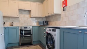 A compact kitchen with a washing machine, oven, and microwave. - Linhay Barn (Saltash)