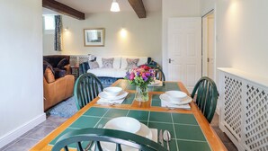 A dining area with a wooden table set for four, green chairs, and a floral centerpiece. - Linhay Barn (Saltash)