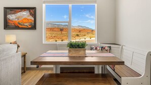 A dining area with a wooden table, bench seating, a window with a desert view, and a framed artwork on the wall. - American Dreams: Prime Location by Pool! (Hurricane)