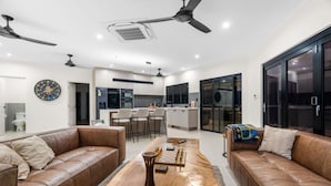 A modern living room with leather sofas, a wooden coffee table, and a kitchen in the background. - Zenlux Mermaid Sunsets Beachfront Fishing Retreat (Dundee Beach)