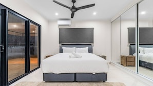 A modern bedroom with a large bed, a ceiling fan, and a sliding glass door. - Zenlux Mermaid Sunsets Beachfront Fishing Retreat (Dundee Beach)