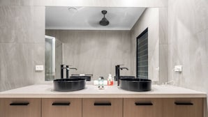 A modern bathroom with two black sinks, a mirror, and a ceiling fan. - Zenlux Mermaid Sunsets Beachfront Fishing Retreat (Dundee Beach)