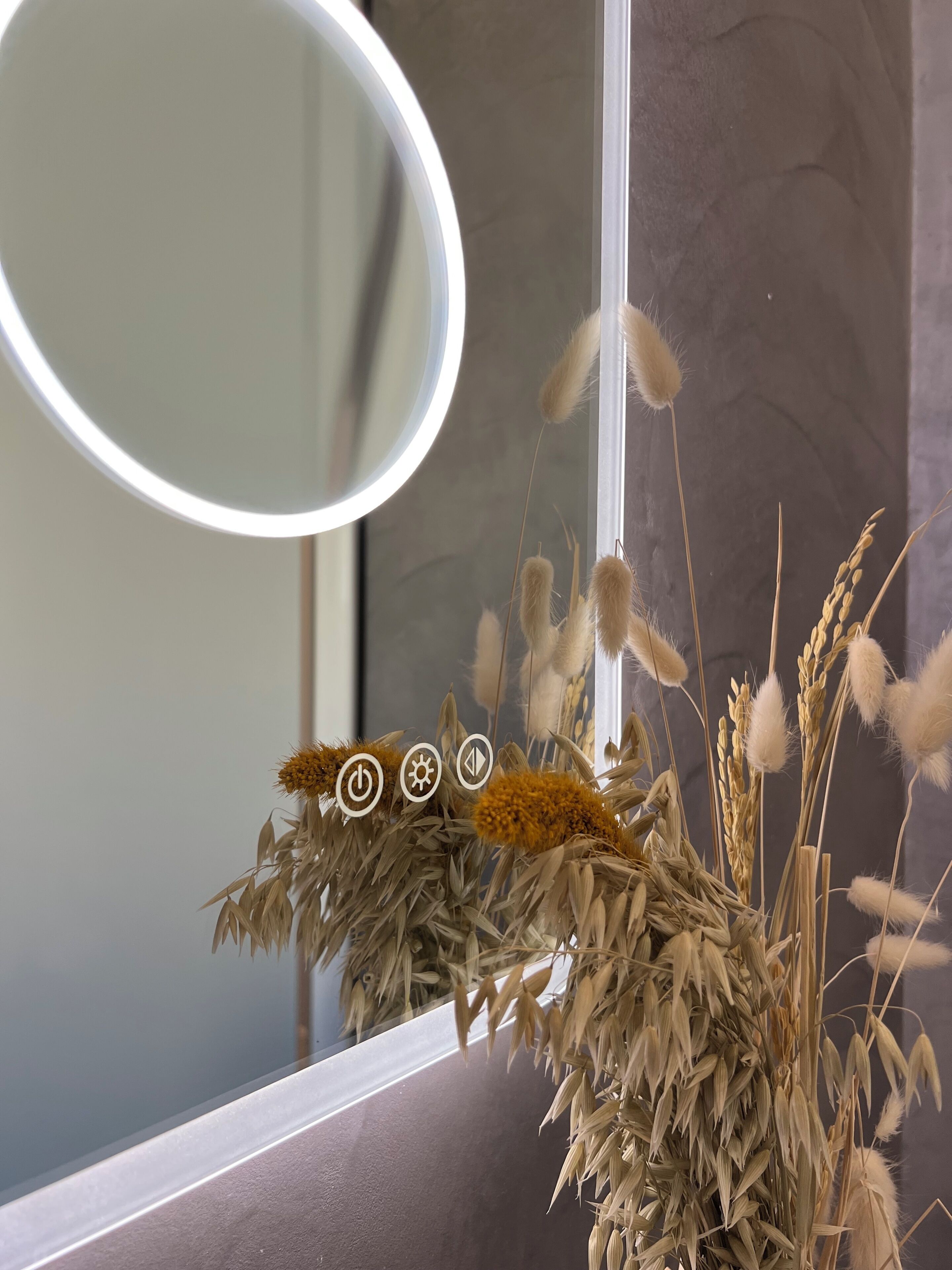 Ein Badezimmer mit Spiegel, einer Vase mit Trockenpflanzen und einer Wand mit Strukturmuster.
