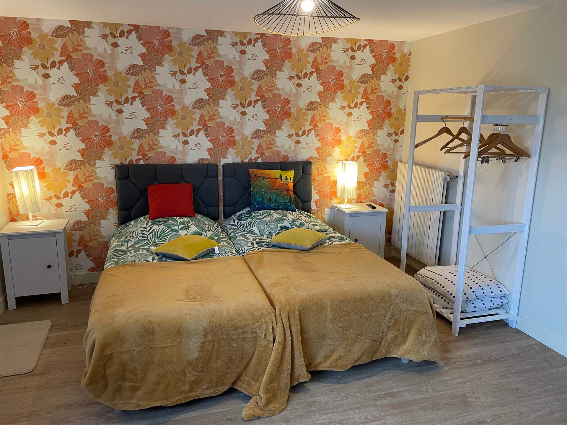 Un lit double avec une tête de lit à motifs floraux, deux lampes de chevet, une armoire suspendue et un radiateur.