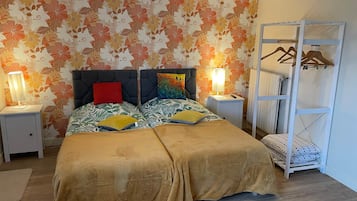 Un lit double avec une tête de lit à motifs floraux, deux lampes de chevet, une armoire suspendue et un radiateur.