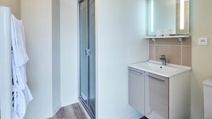 Un bany modern amb plat de dutxa de vidre, un lavabo blanc i un mirall a sobre.