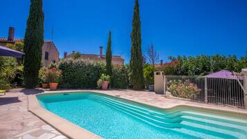 Una piscina con baldosas de piedra, rodeada de plantas en macetas y altos árboles.
