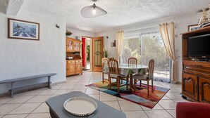 A dining area with a table, chairs, a bench, a television, and a ceiling fan. - La Thébaïde – 3-Star Villa with Private Pool near Fréjus-St-Raphaël (Puget-sur-Argens)
