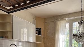 A kitchen with white cabinets, a wooden countertop, a sink, a microwave, and a dining area with a glass table and chairs. - A cozy 35 m² apartment near Montmartre (Paris)