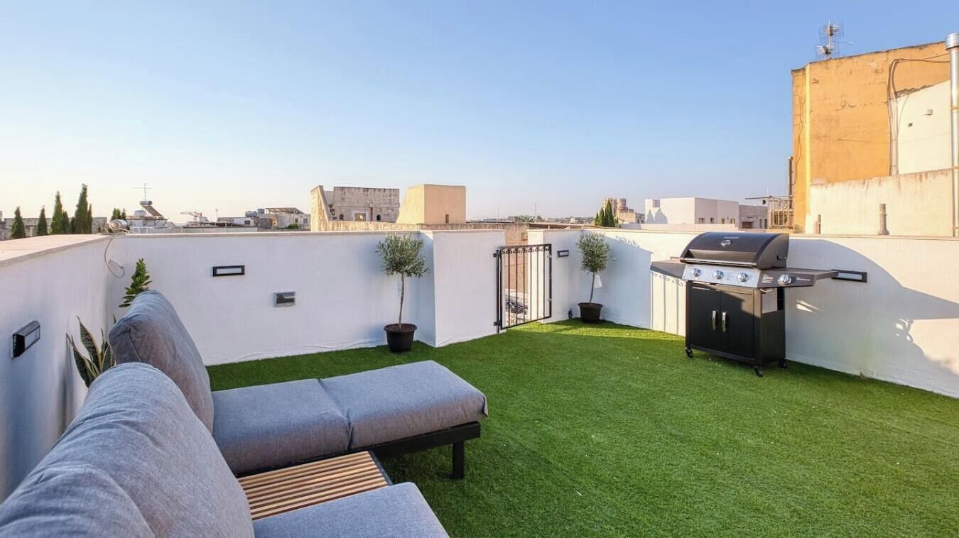 A rooftop terrace with a grill, a sofa, and a small lawn.