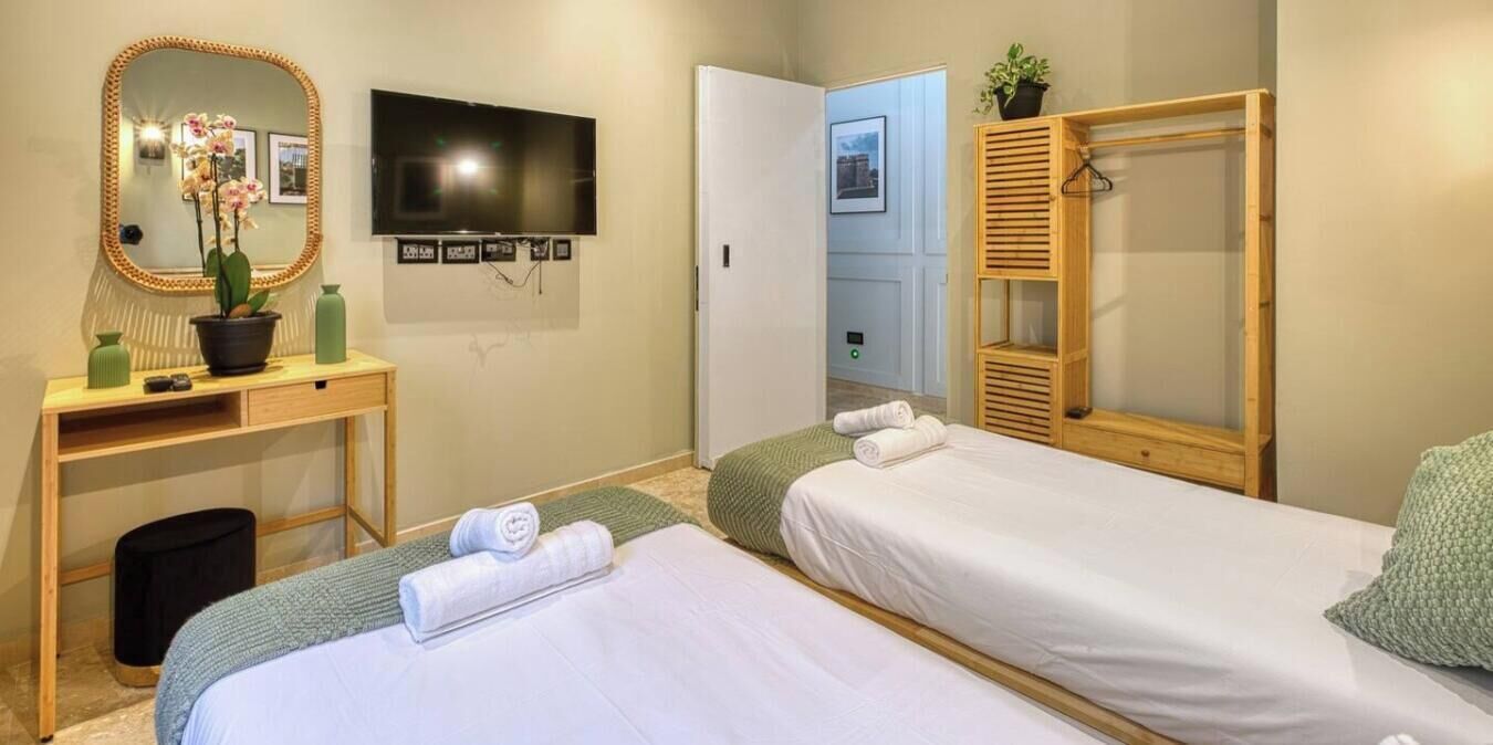 Ein Hotelzimmer mit zwei Betten, einem Schreibtisch mit Spiegel, einem Fernseher und einer Tür zu einem anderen Raum.