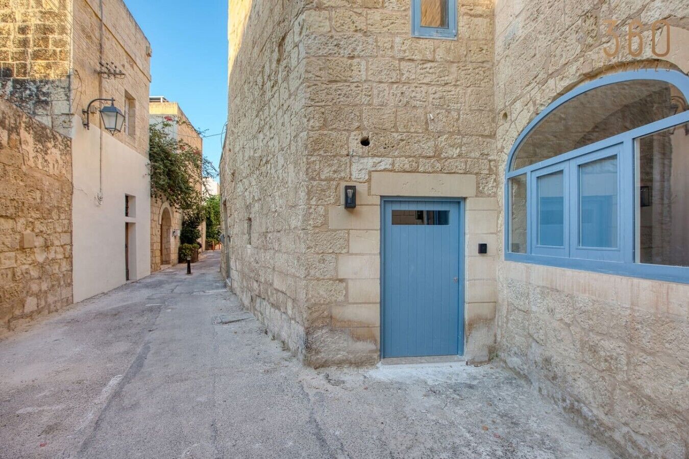 A narrow street with stone buildings, a blue door, and a window with a blue frame.