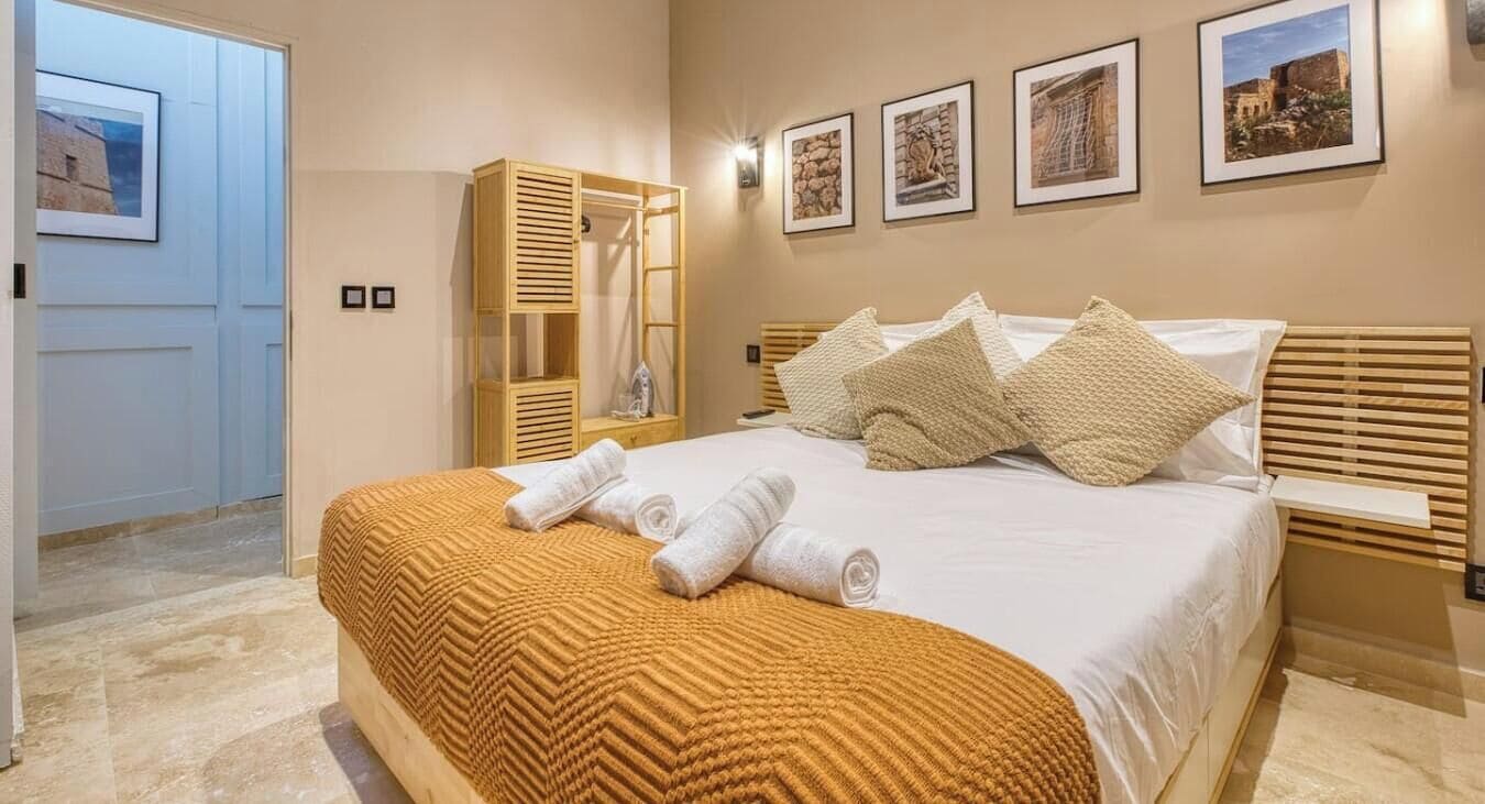 A neatly arranged bedroom with a bed, a wooden wardrobe, and a wall with framed pictures.
