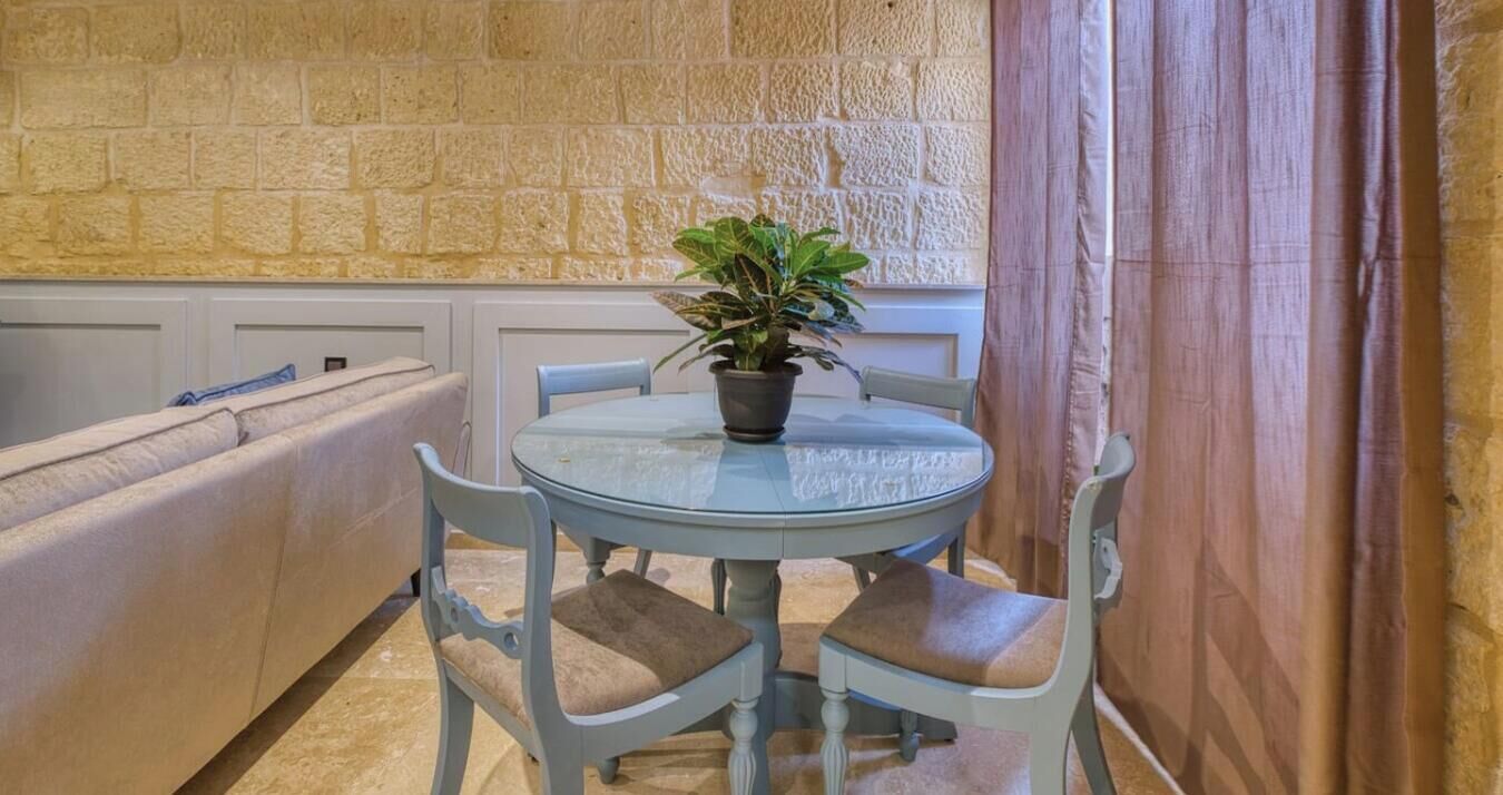 A round glass table with four chairs, a potted plant, and a stone wall in the background.
