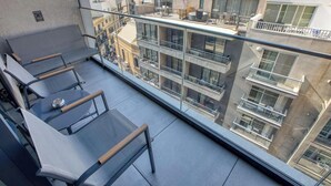 Een balkon met glazen hekwerk, een tafel en twee stoelen.