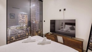 Hotelkamer met een bed, een televisie, een houten dressoir en een groot raam met uitzicht op de stad.