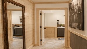 A corridor with wooden walls, a tiled floor, and a door leading to a kitchen area. - Studio on the River! (Noel)