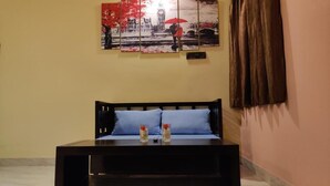 Una habitación con una cama, una mesa de centro de madera oscura con dos jarrones, un cuadro colgado en la pared y una lámpara.