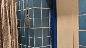 Un ascensor con paneles azules, un tablero de control metálico, una puerta blanca y botones de metal.